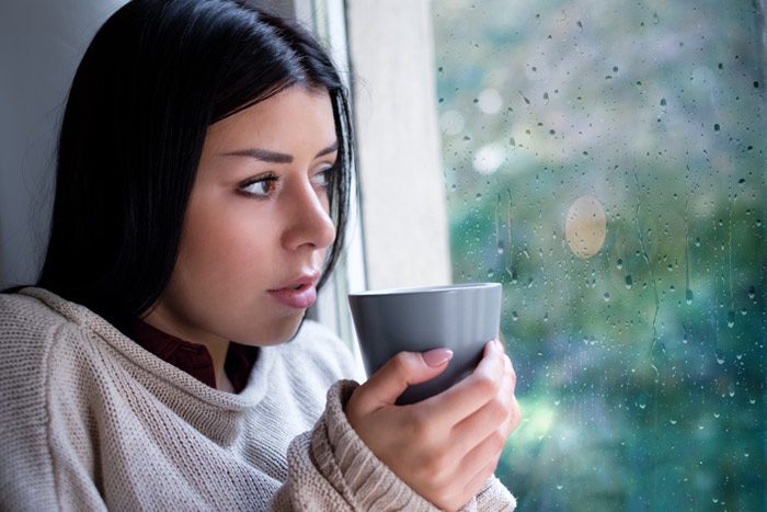 beautiful dark-haired young woman looks out the window while drinking coffee - seasonal affective disorder